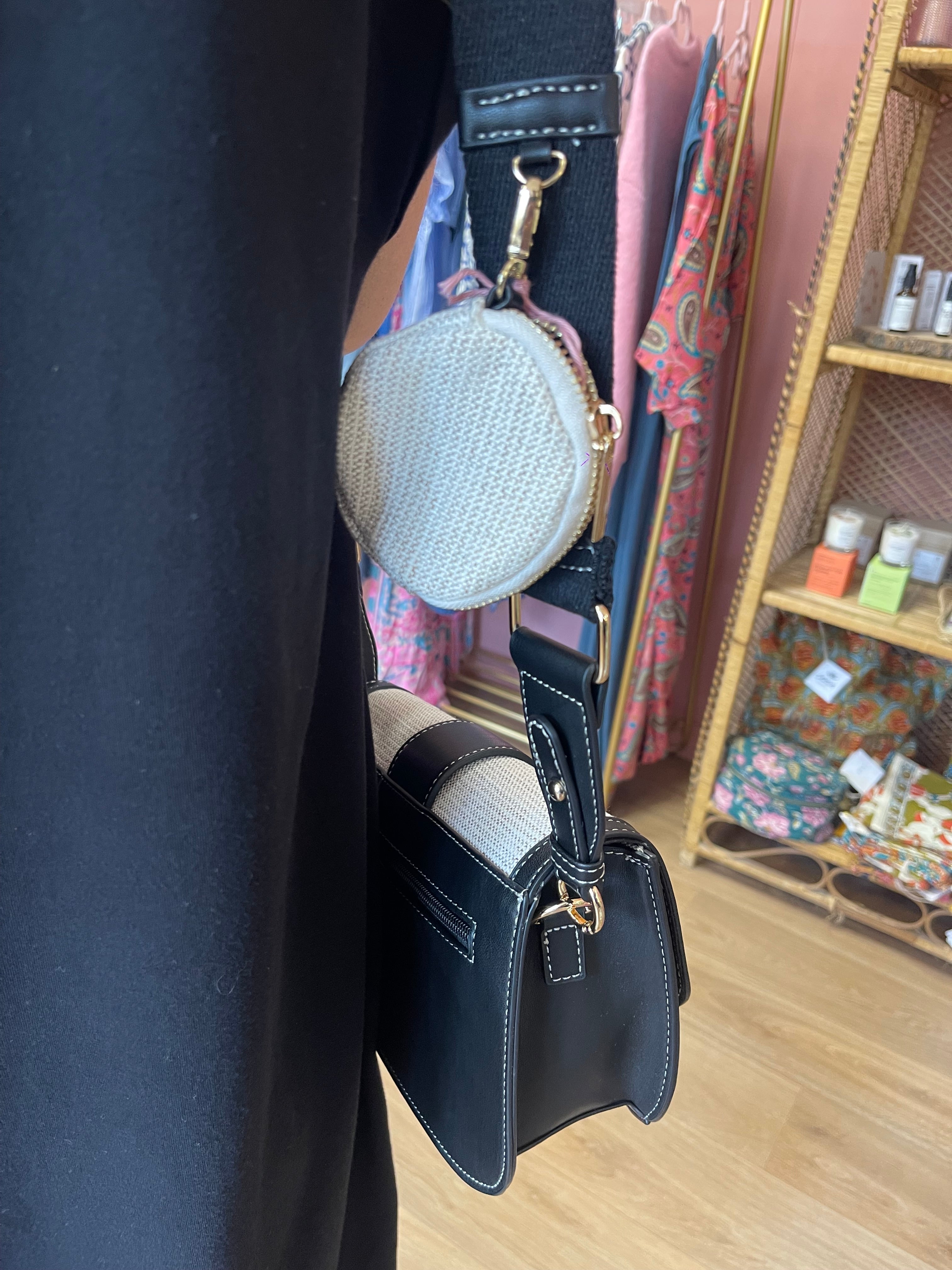 Vue de côté du sac à bandoulière noir et blanc, montrant une petite pochette ronde attachée à la sangle noire du sac.