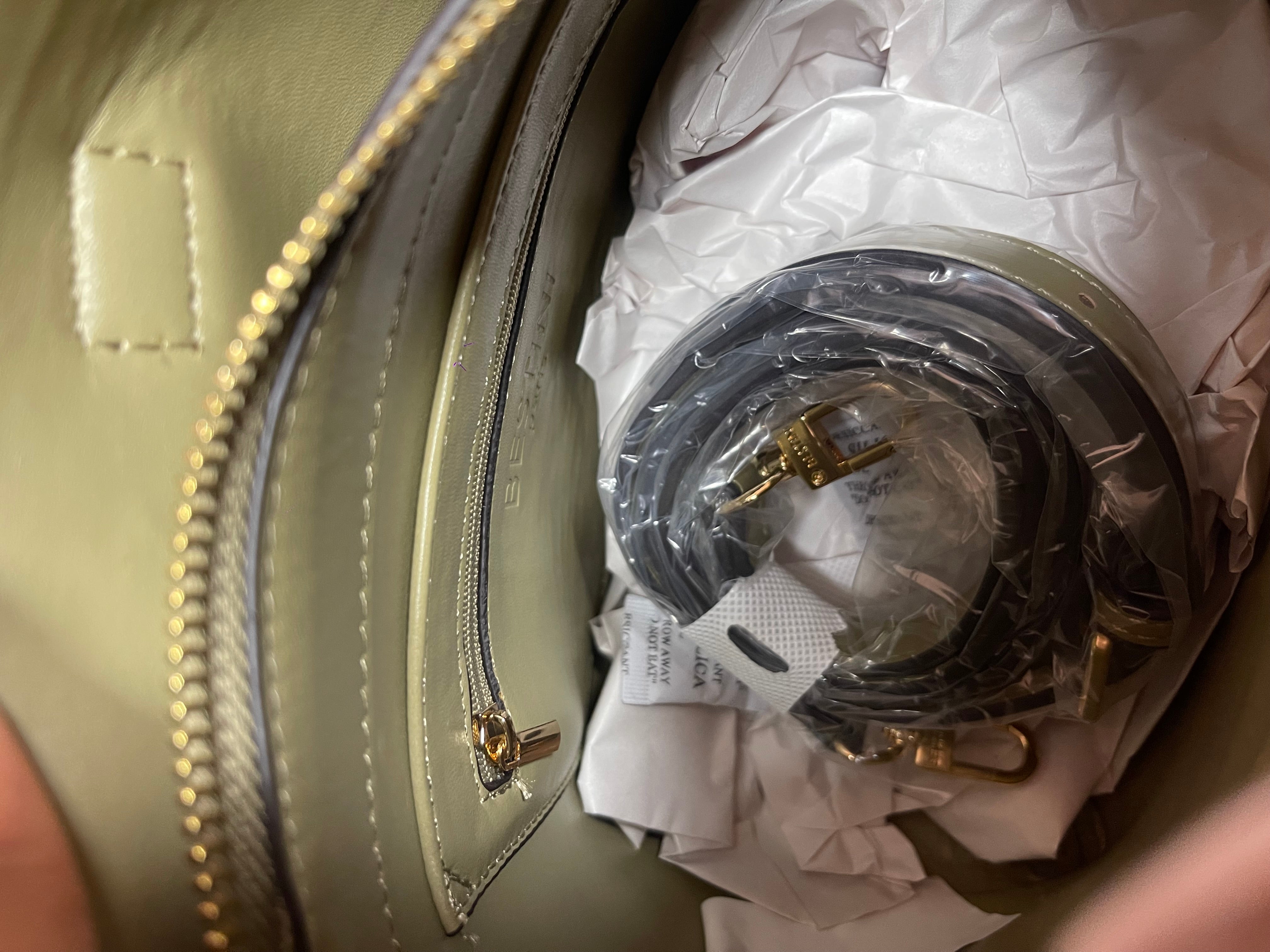 Vue de l’intérieur du sac PISE vert olive montrant une poche zippée interne et une bandoulière supplémentaire emballée en plastique.